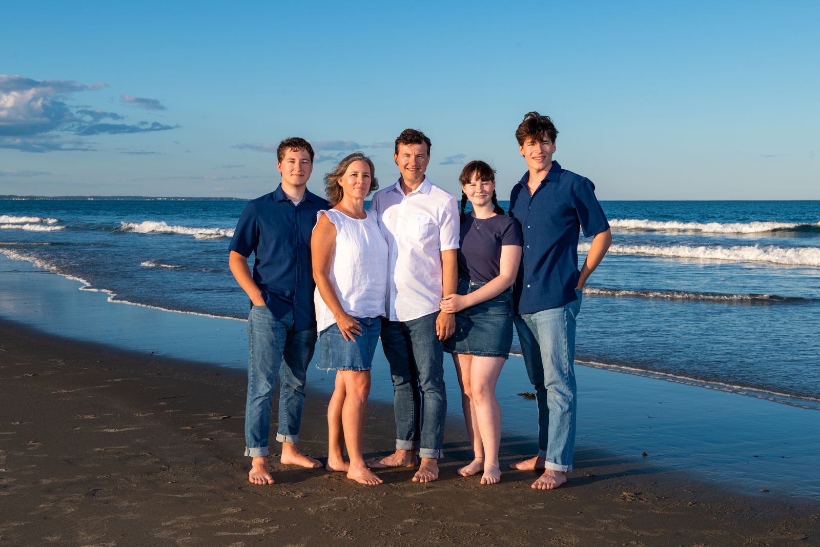 Family of five standing barefoot on a beach at golden hour