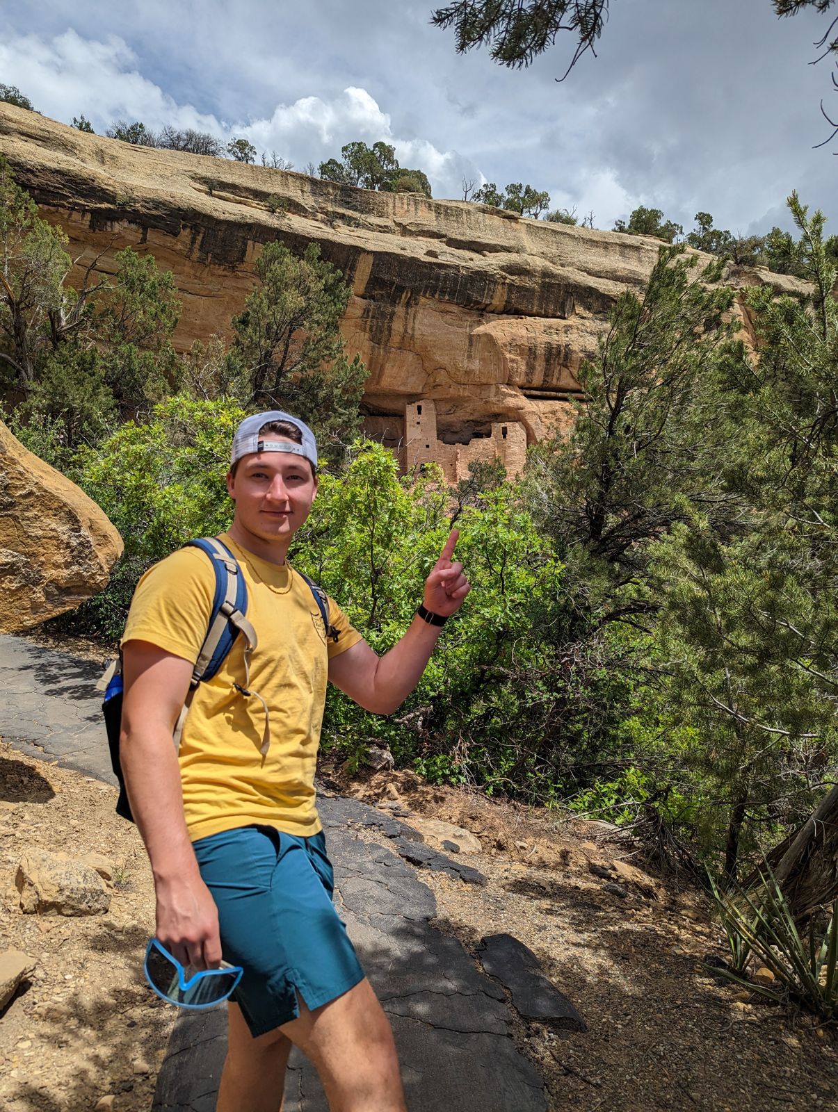 Hiker on a trail with cliff dwellings in the rock above