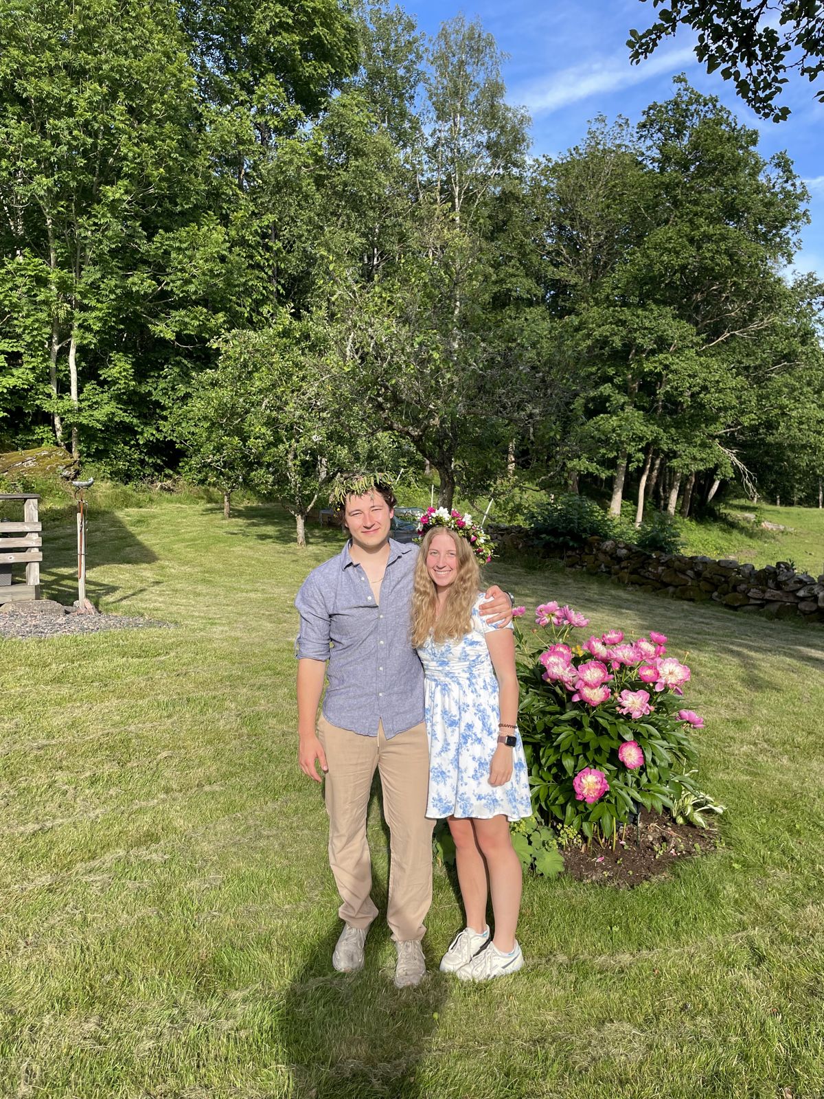 Couple standing on a lawn beside a peony bush