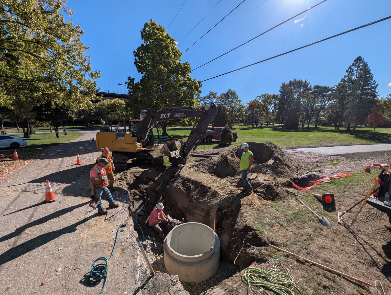 Crew setting a manhole section in an open trench beside a road