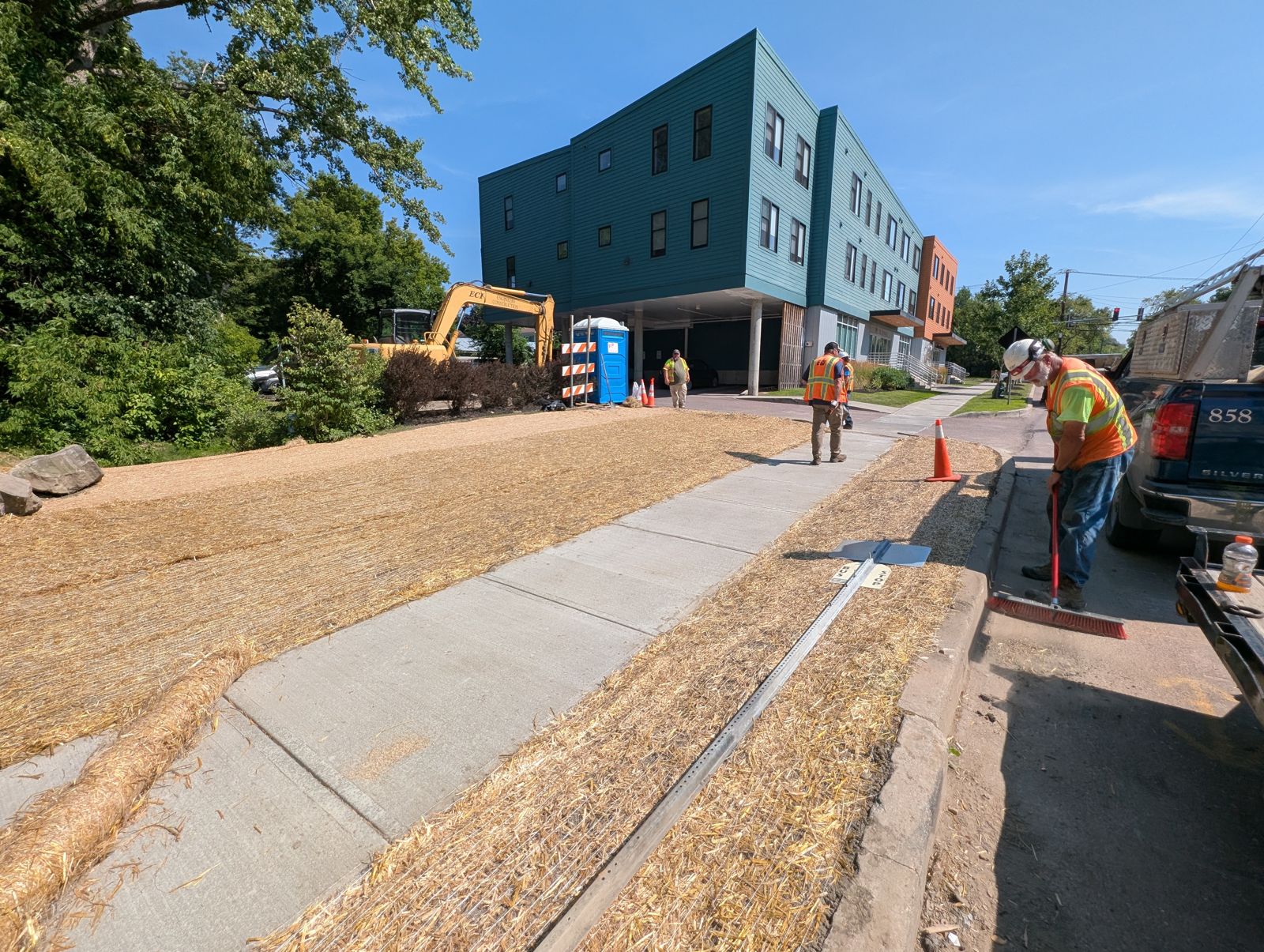 New sidewalk with straw-covered slopes in front of a building under construction