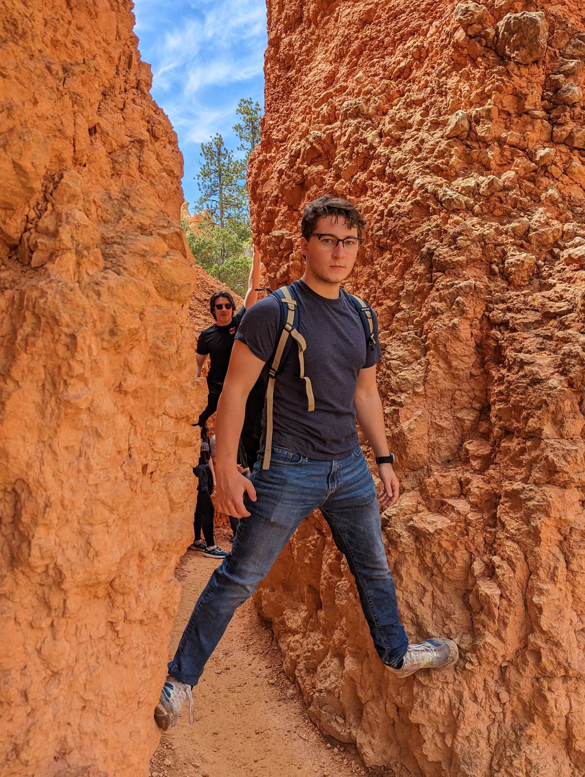 Hiker bracing across a narrow orange slot canyon