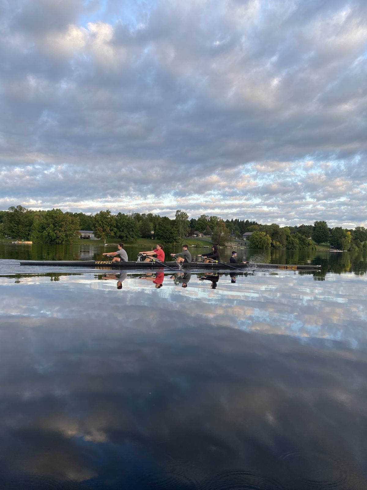 Rowing shell on glassy water reflecting a cloudy sky